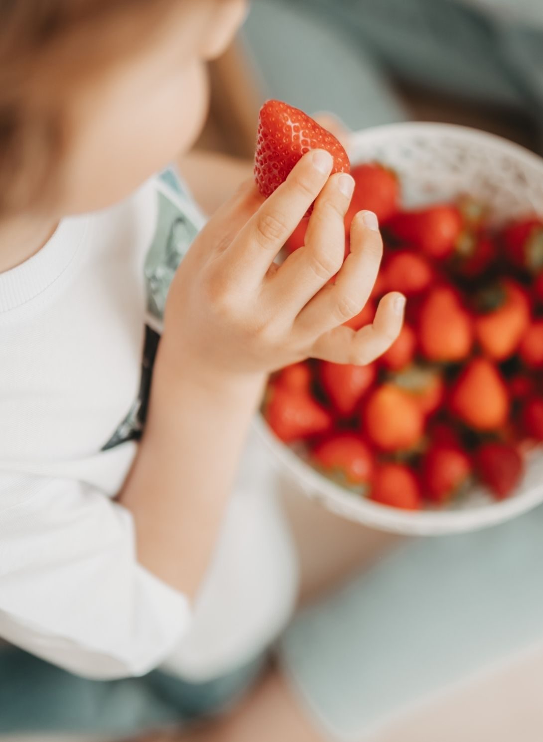 Kind hält eine frische Erdbeere, während eine Schale voller Erdbeeren gereicht wird – Symbolfoto für Familiengesundheit im Rahmen der Familienberatung in Salzburg mit Sibylle Paier.